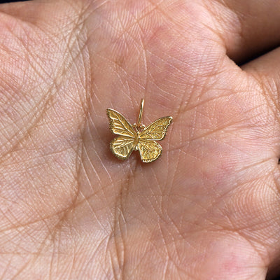 A solid gold Butterfly Charm for chain resting in a model's palm