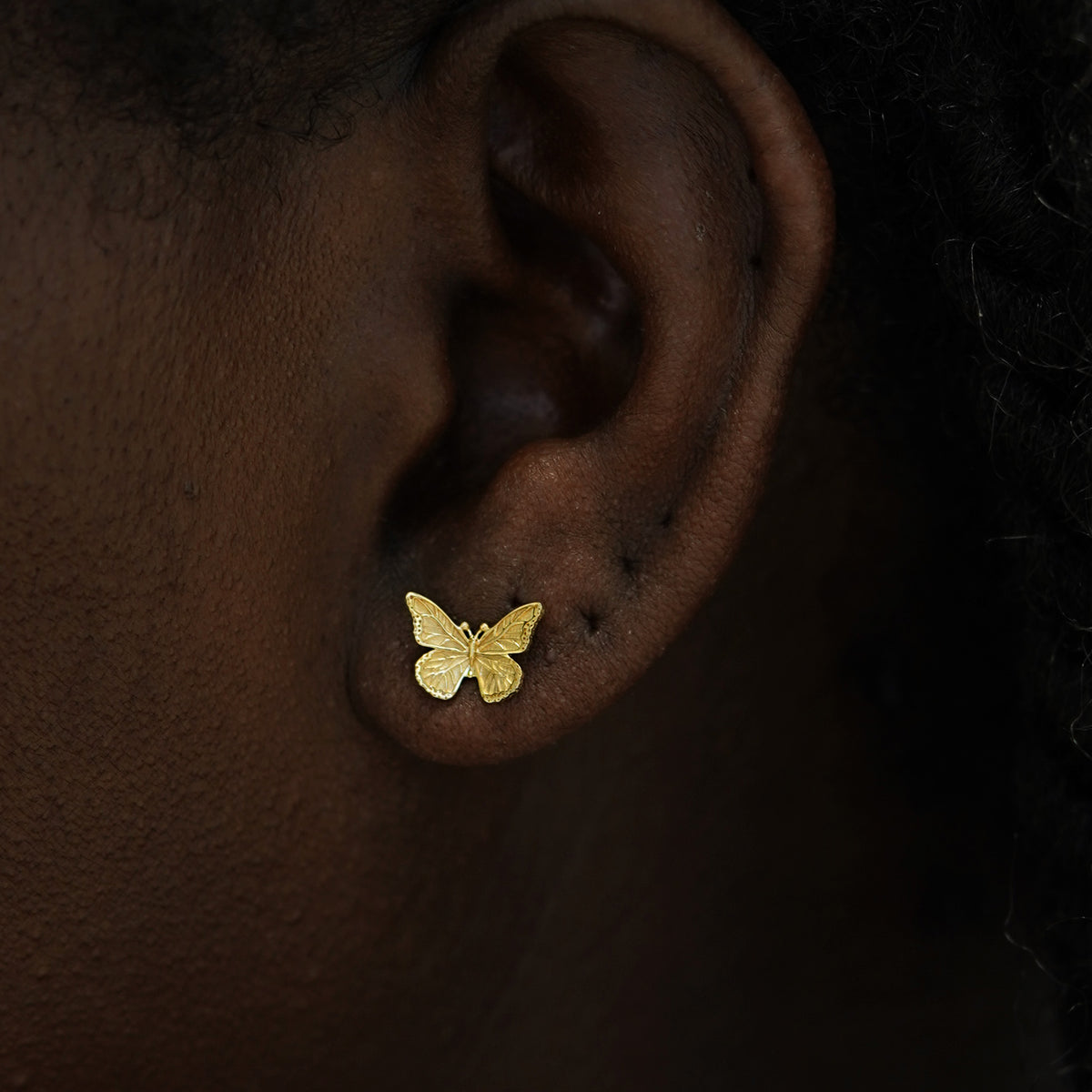 Close up view of a model's ear wearing a 14k gold Butterfly Earring