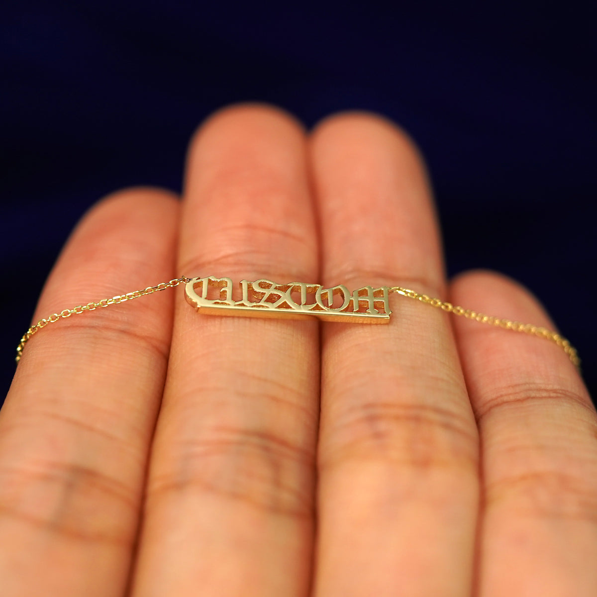 A 14k yellow gold small custom nameplate necklace laying flat on a model's fingers to show the thickness of the letters
