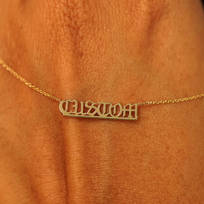 A solid yellow gold small custom nameplate necklace draped over the back of a model's hand