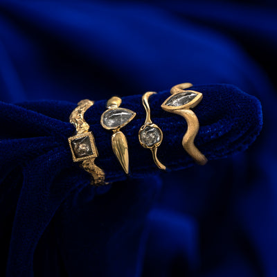 Four engagement rings with different shapes of cabochon salt and pepper diamonds stacked sideways on a blue cloth