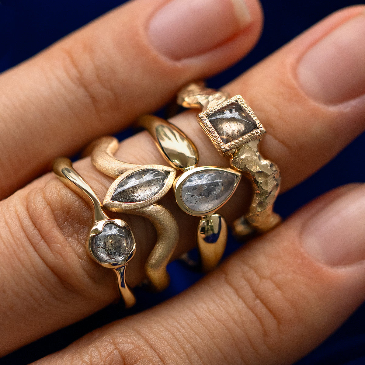 Four engagement rings with different shapes of cabochon salt and pepper diamonds stacked on a model's finger