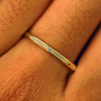 Close up view of a model's fingers wearing a yellow gold 2mm Curvy Mirror Band with one diamonds