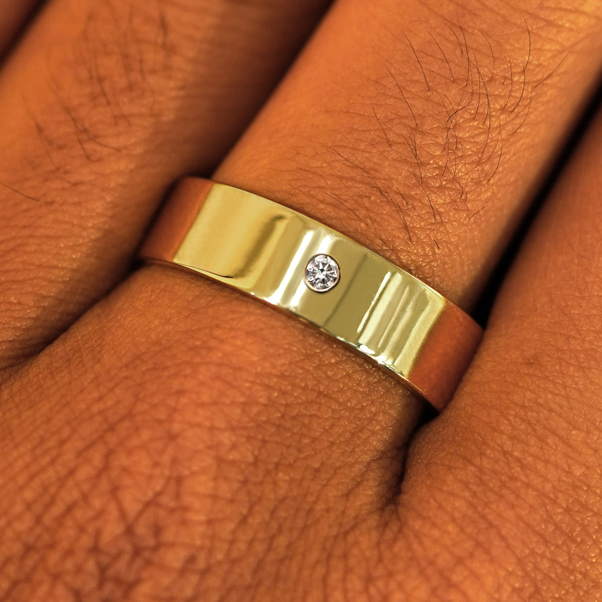 Close up view of a model's fingers wearing a 14k yellow gold Industrial Mirror Band with center diamond