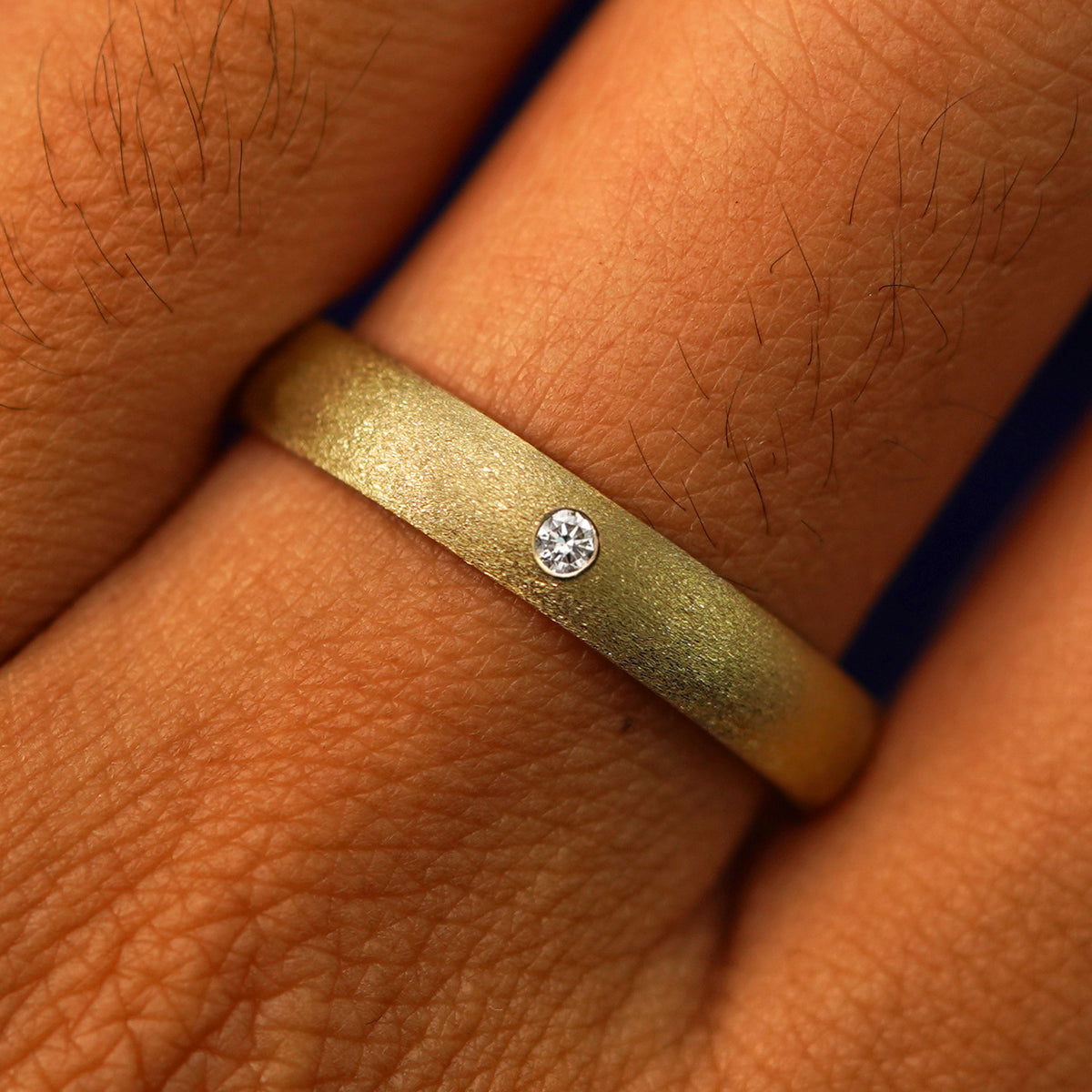 Close up view of a model's fingers wearing a 14k yellow gold Curvy Stardust Band with center gem