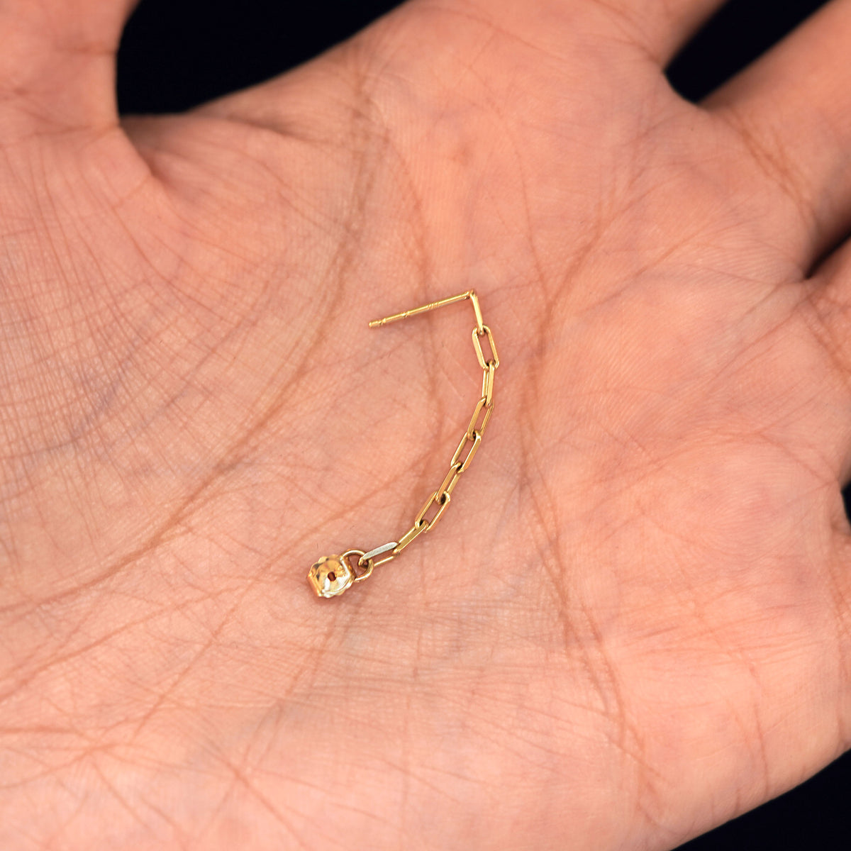 A solid yellow gold Butch Chain Loop with the backing unattached to post sitting in a model's hand