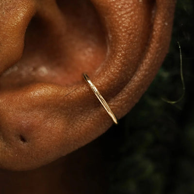 Close up view of a model's ear wearing a solid 14k champagne gold Line Cuff
