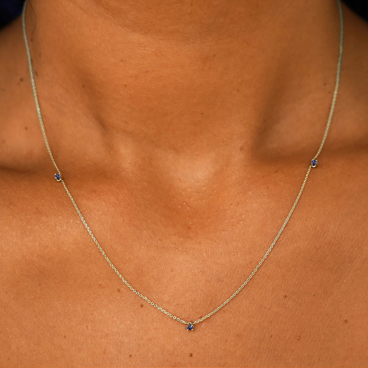Close up view of a model's neck wearing a solid 14k champagne gold 3 Gemstone Cable Necklace in sapphire