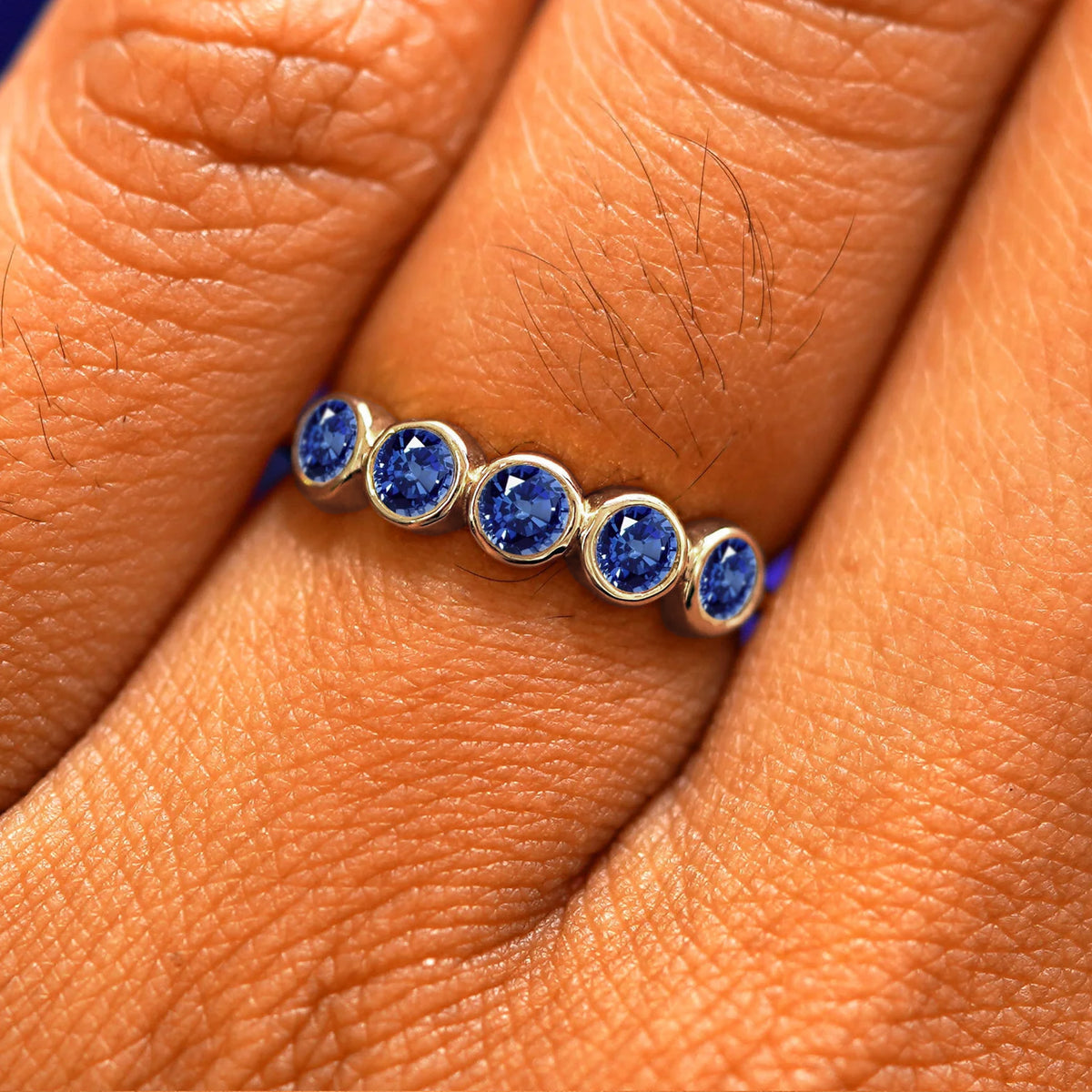 Close up view of a model's hand wearing a champagne gold 5 Gemstones Ring in sapphire