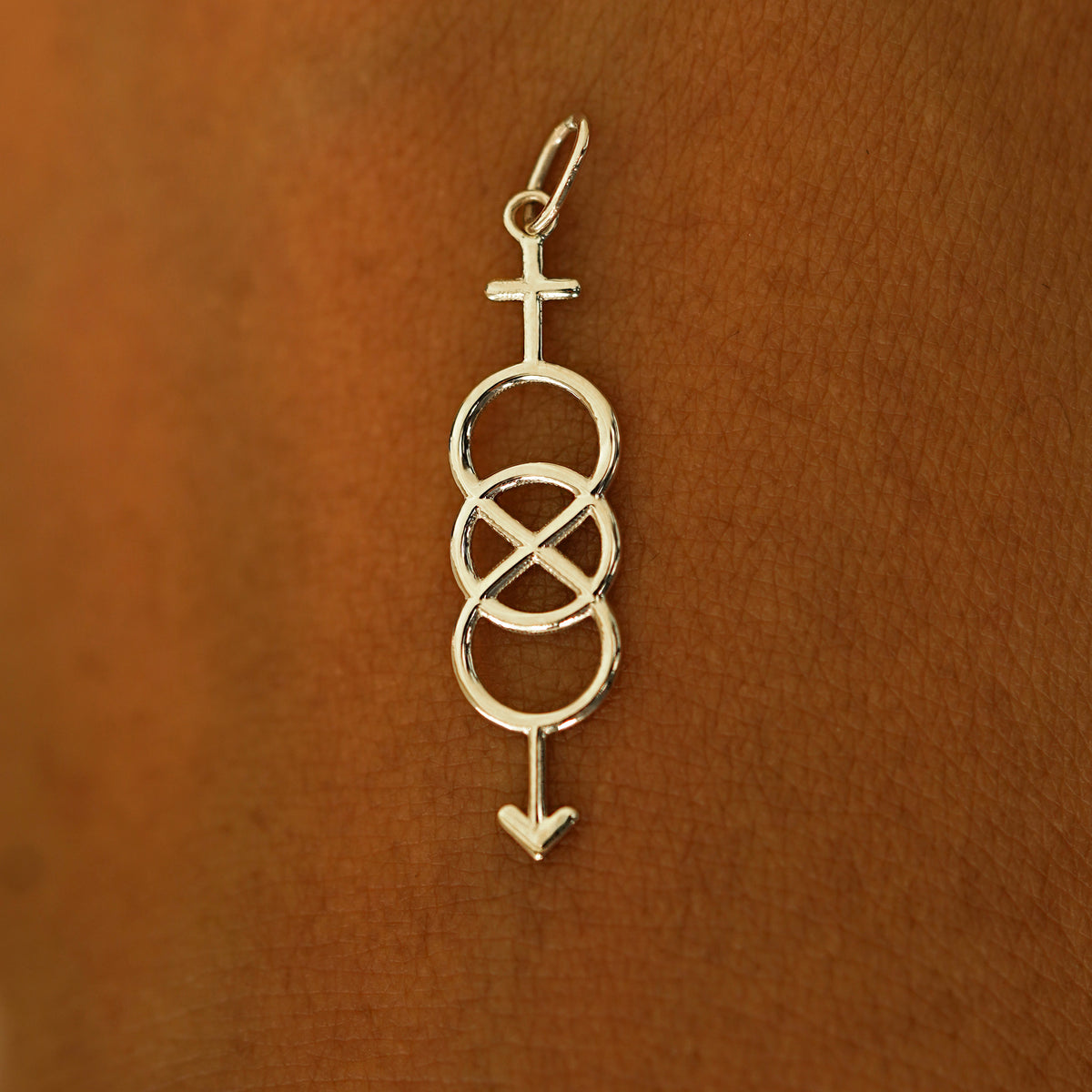 A solid 14k champagne gold Bisexual Symbol Charm resting on the back of a model's hand