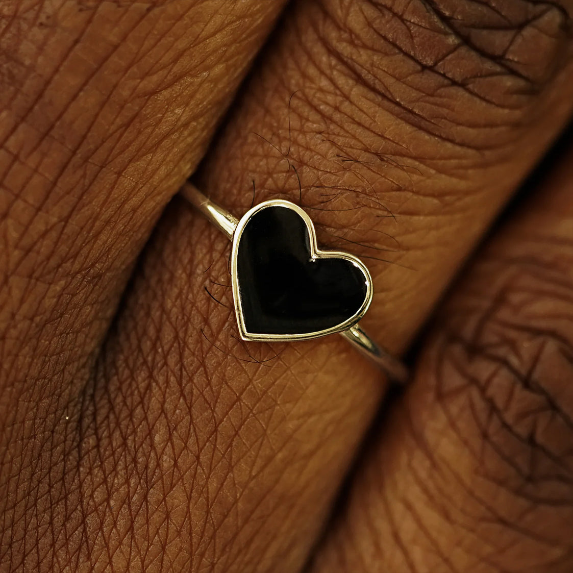 Close up view of a model's fingers wearing a 14k champagne gold black enamel heart ring