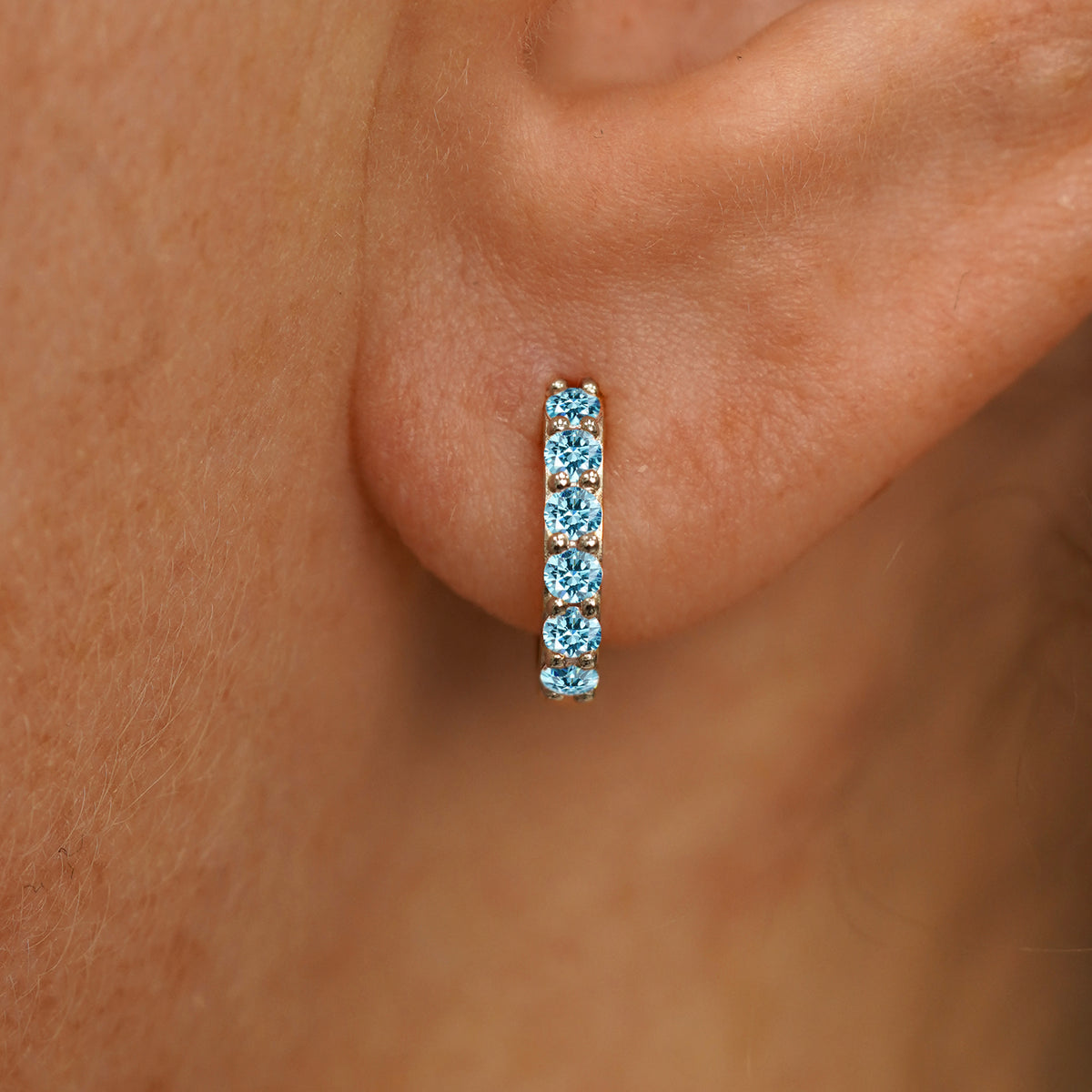 Close up view of a model's ear wearing a champagne gold Small Light Blue Lab Diamond Huggie Hoop