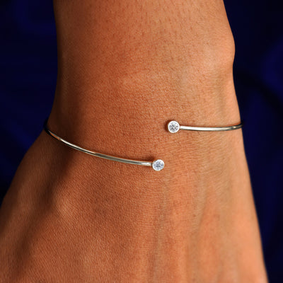 Close up view of a model's wrist wearing a 14k champagne gold clear diamond gemstone bypass bangle
