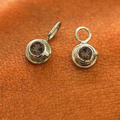 A solid champagne gold coffee cup charm resting on a back of the model's hand