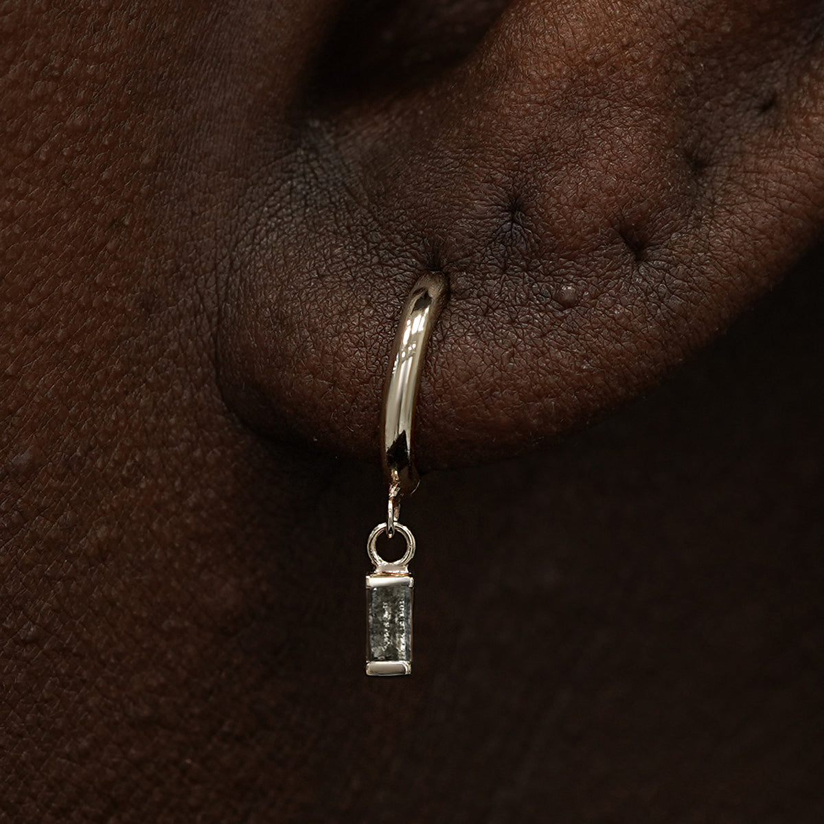 Close up view of a model's ear wearing a champagne gold Baguette Diamond Dangle Huggie Hoop