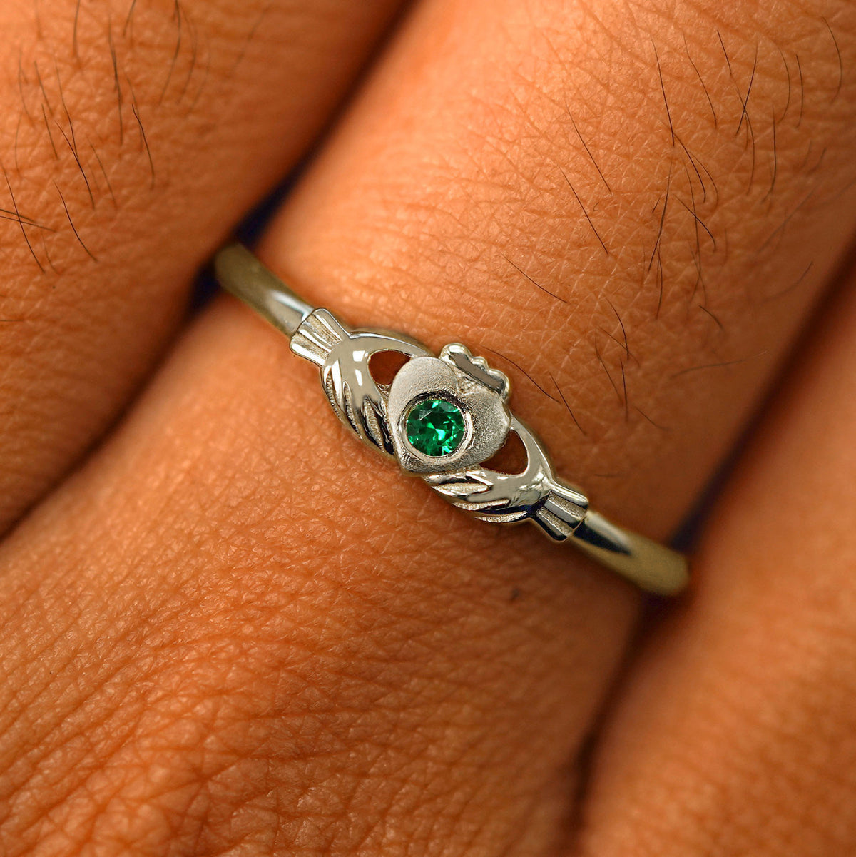 Close up view of a model's fingers wearing a 14k champagne gold emerald Thin Gemstone Claddagh Ring