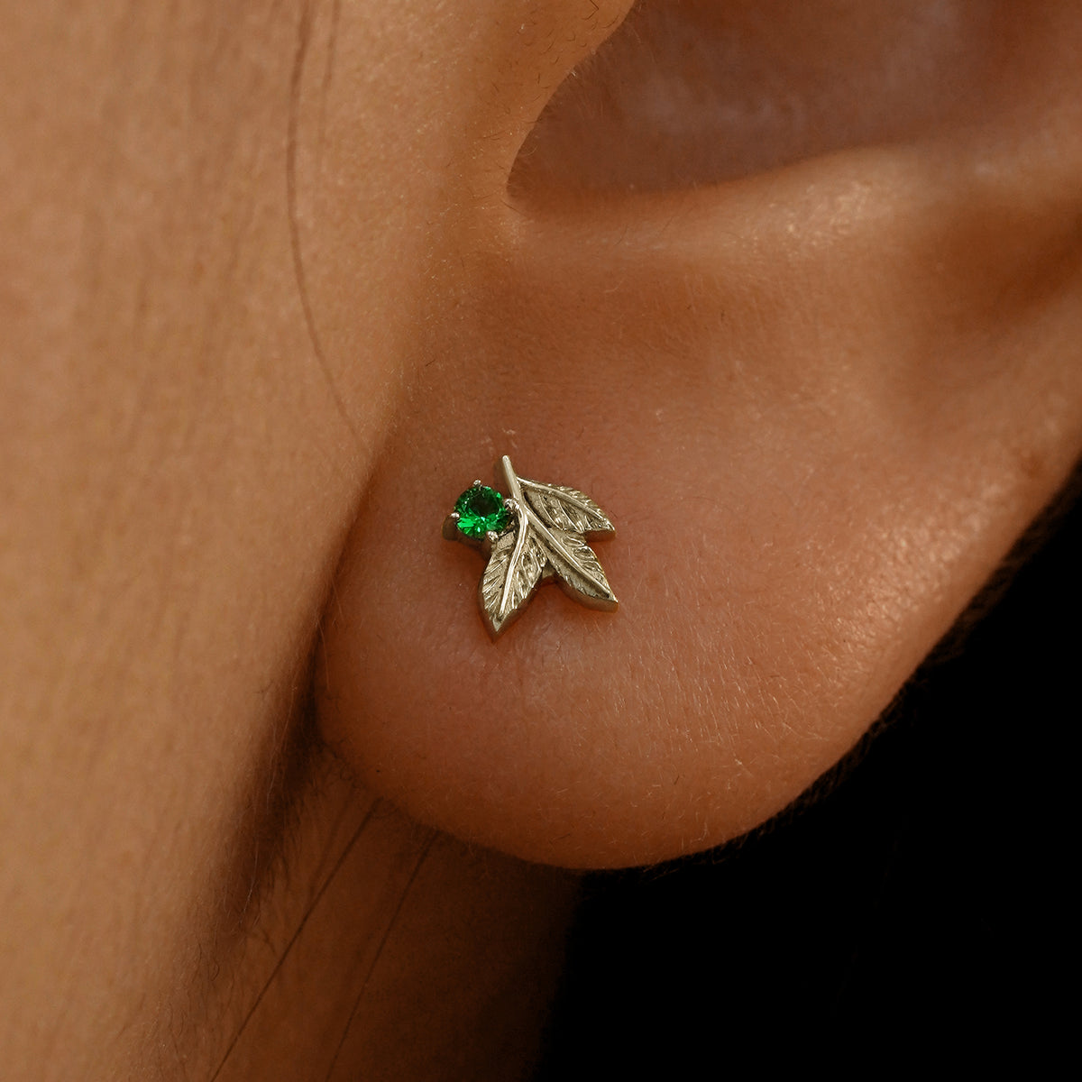Close up view of a model's ear wearing a 14k champagne gold emerald 3 Leaves Gemstone Earring