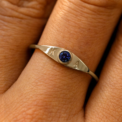 A model's finger wearing a sapphire yellow gold gemstone monogram ring with the initials K A
