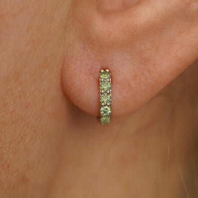 Close up view of a model's ear wearing a champagne gold Mini Light Green Lab Diamond Huggie Hoop