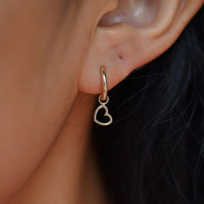 Close up view of a model's ear wearing a champagne gold Heart Charm on a Curvy Huggie Hoop