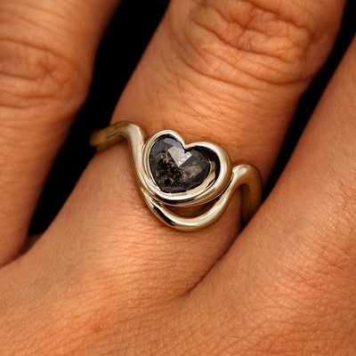 A model's hand wearing a 14k champagne gold Heart Salt and Pepper Diamond Infinite Wave Ring