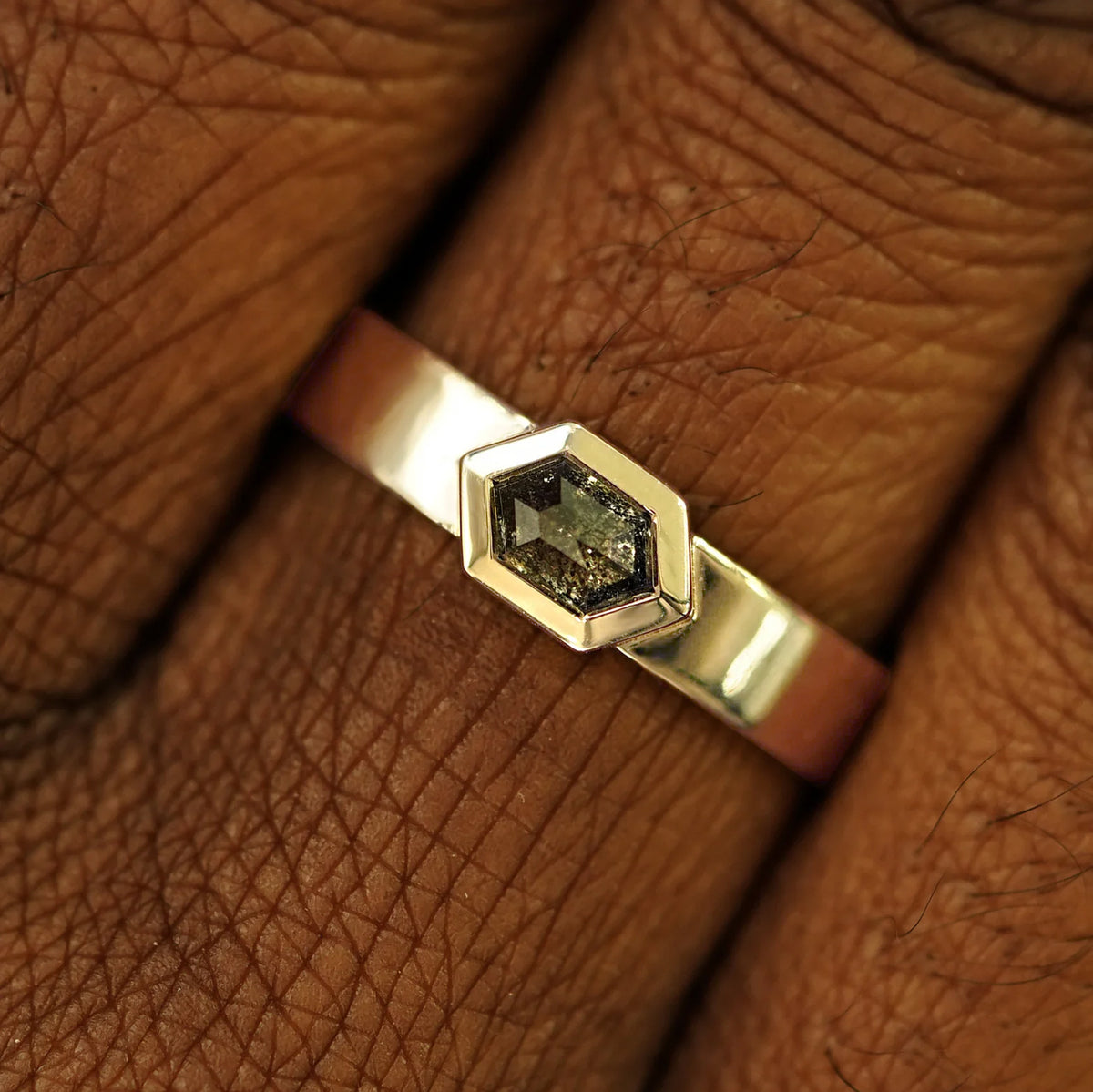 Close up view of a model's hand wearing a solid champagne gold Hexagon Diamond Band