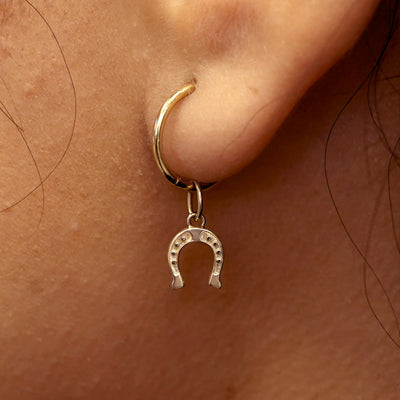 Close up view of a model's ear wearing a champagne gold Horseshoe Charm on a Small Seamless Huggie Hoop
