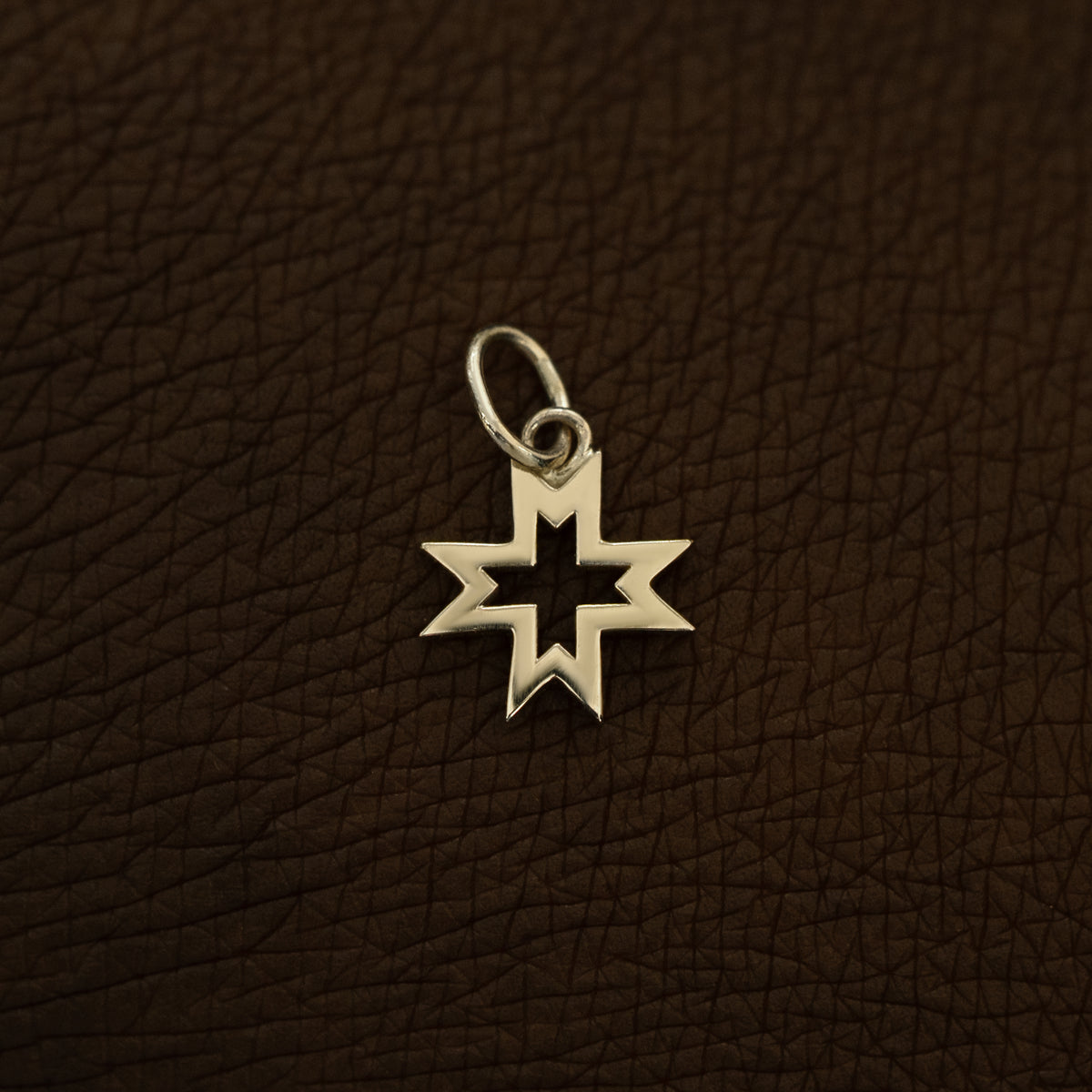 A 14 karat champagne solid gold Large Open 8 Pointed Star Charm on the back of a model's hand
