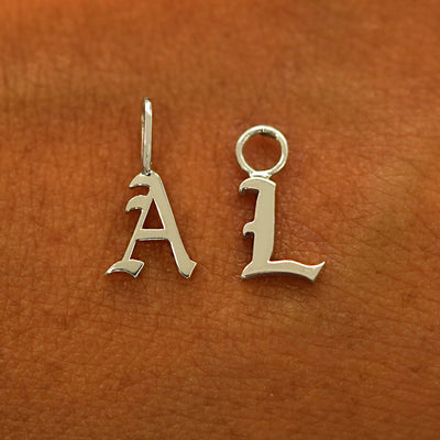 A 14k champagne gold Initial Charm for earring in the letter A and L laying on the back of a model's hand