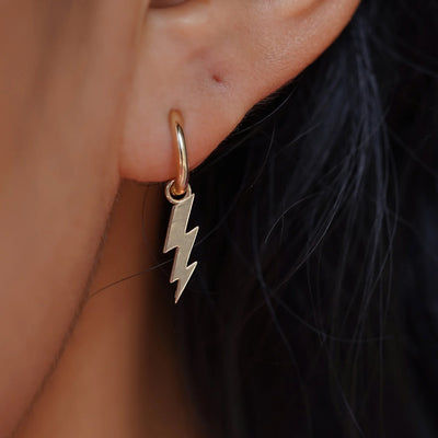 Close up view of a model's ear wearing a champagne gold Lightning Bolt Charm on a Curvy Huggie Hoop