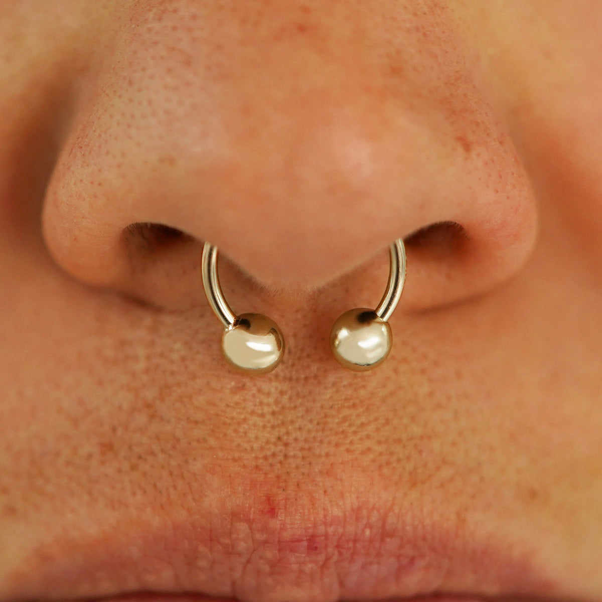 Close up view of a model's nose wearing a 14k champagne gold Medium Horseshoe in a septum piercing