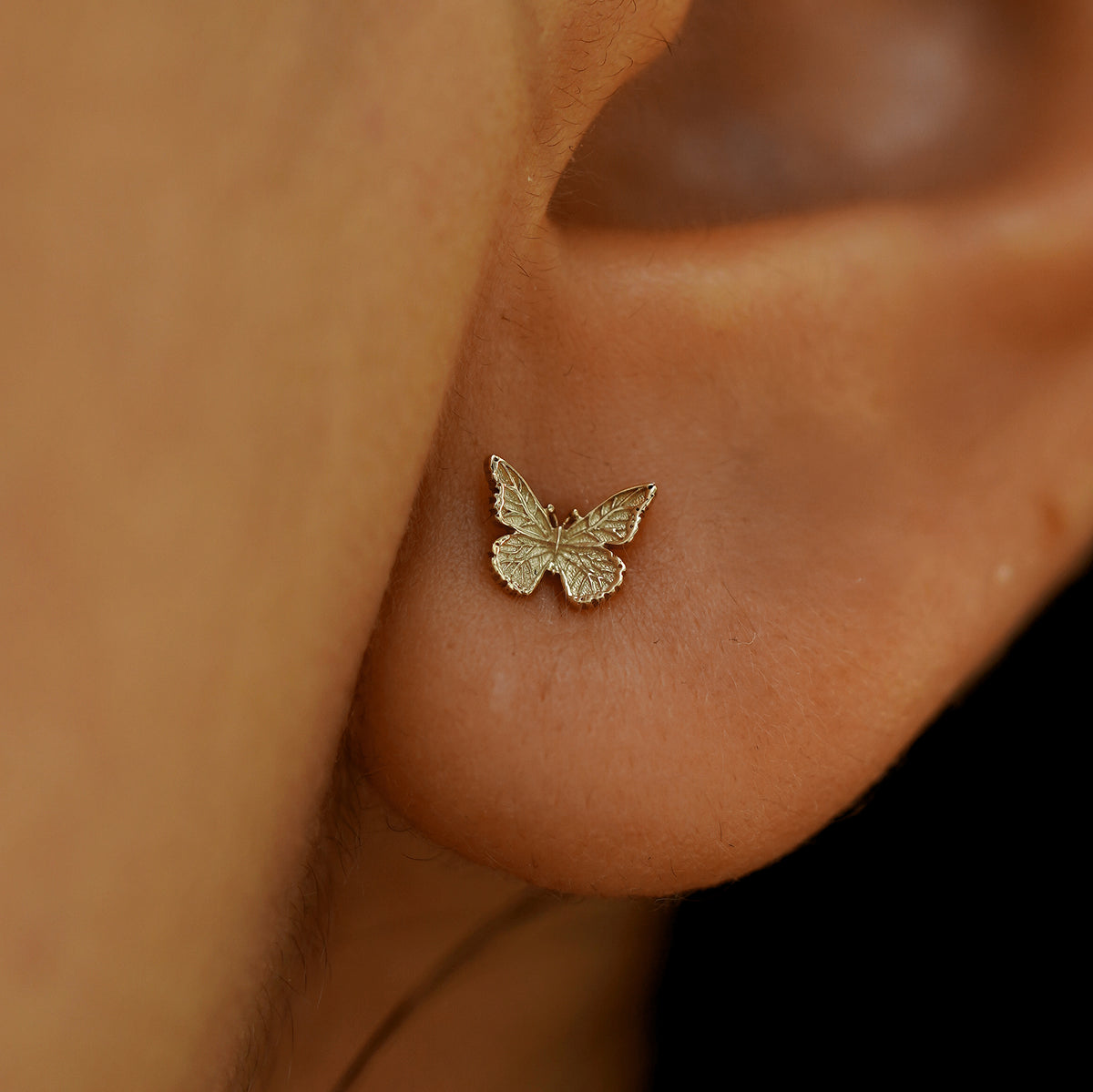 Close up view of a model's ear wearing a 14k champagne gold Mini Butterfly Earring