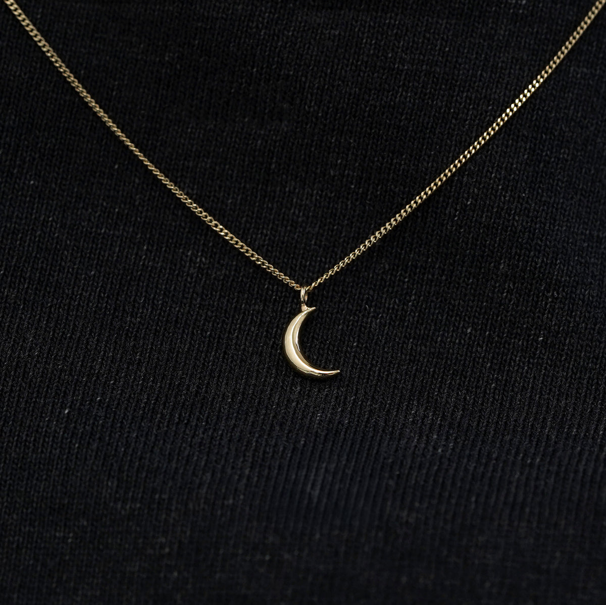 Close up view of a solid 14k champagne gold moon necklace against a model's black shirt