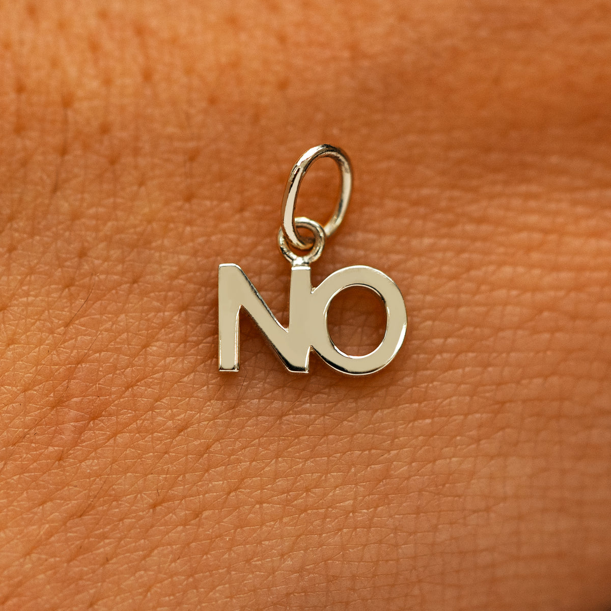 A solid 14k champagne gold No Charm on the back of a models hand