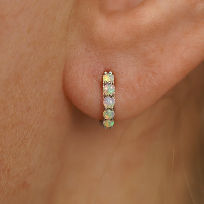 Close up view of a model's ear wearing a champagne gold Mini Opal Huggie Hoop