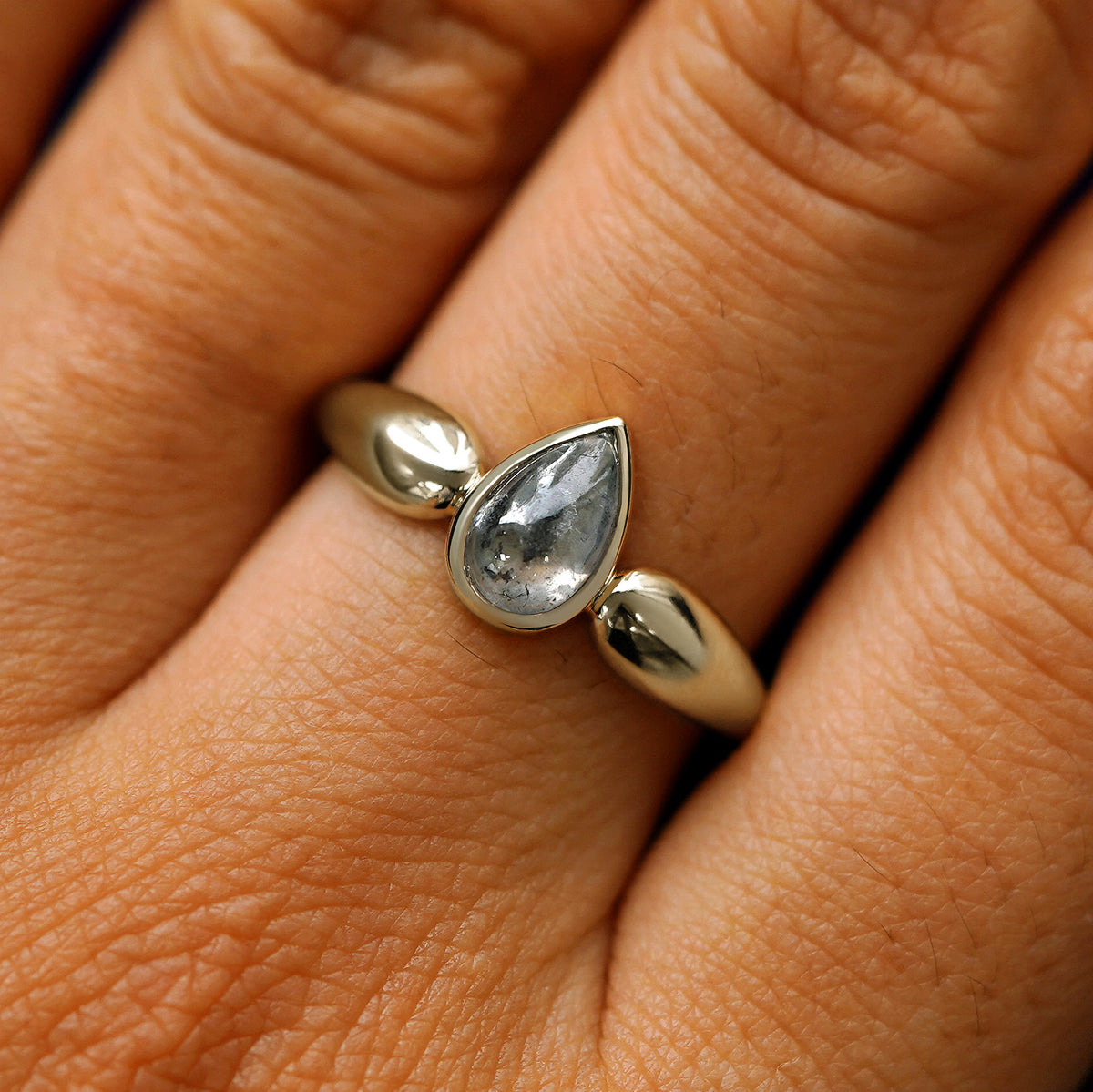 Close up view of a model's hand wearing a 14k champagne gold pear cabochon salt and pepper diamond engagement ring