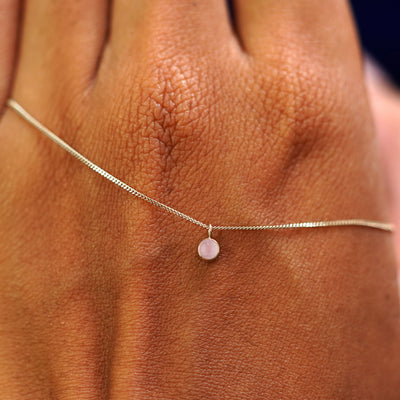 A solid champagne gold Rose Quartz Necklace draped across the back of a model's hand