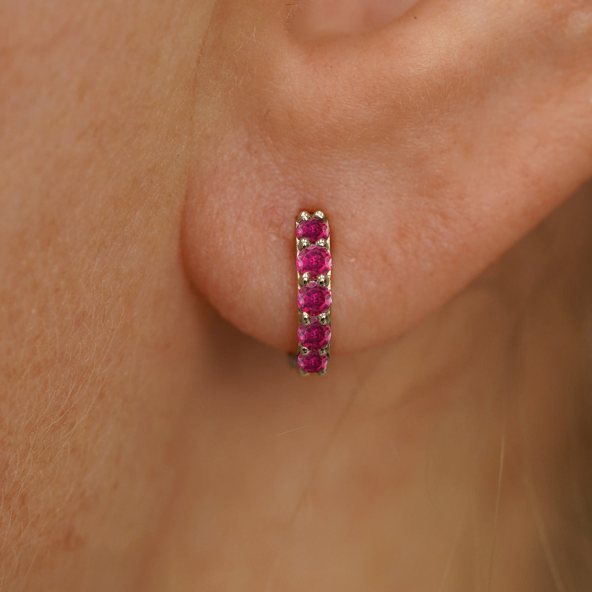 Close up view of a model's ear wearing a champagne gold Mini Ruby Huggie Hoop