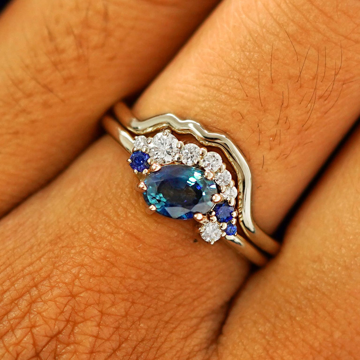 Close up view of a model's fingers wearing a 14k champagne gold Sapphire and Diamond Cluster Ring Set