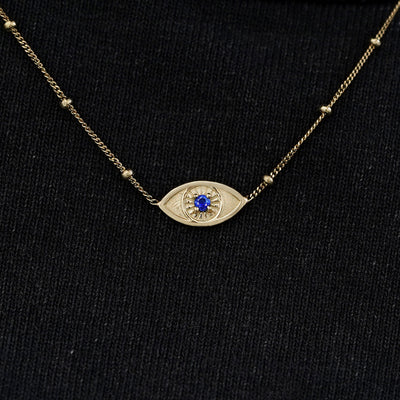 Close up view of a solid 14k champagne gold sapphire evil eye bracelet against a model's black shirt
