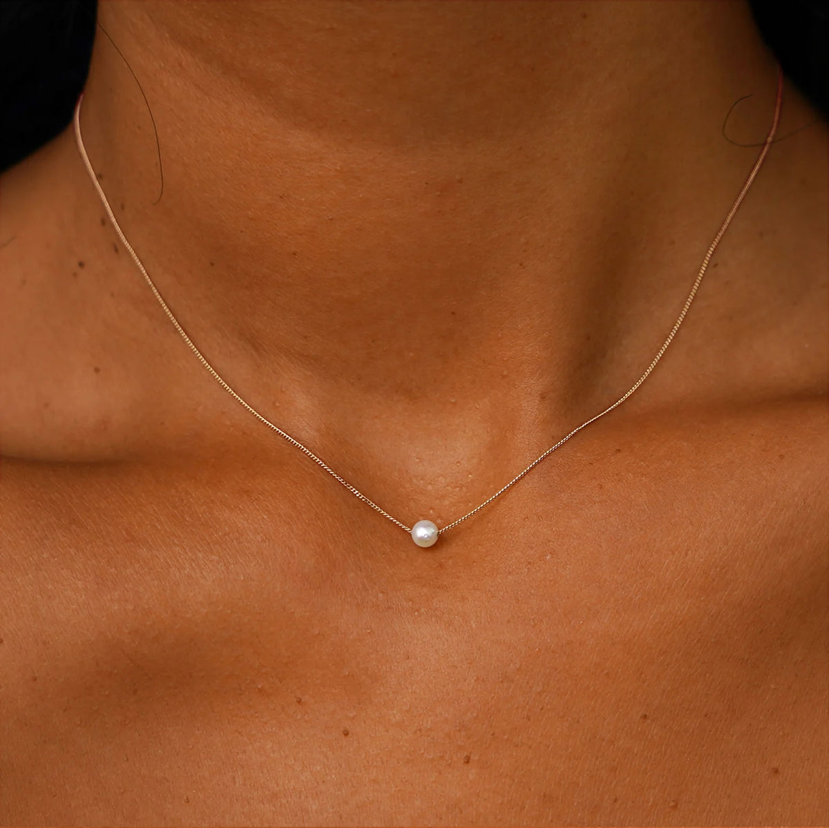 A model's neck wearing a champagne gold Pearl Slide Necklace with a 4mm pearl