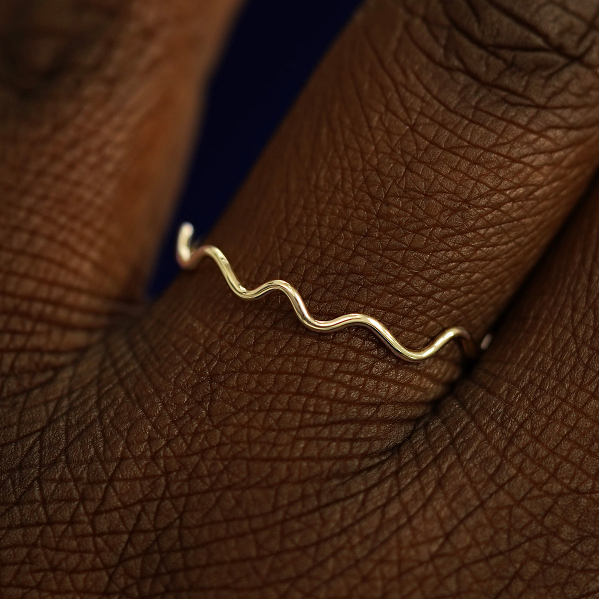 Close up view of a model's hand wearing a solid champagne gold Wave Ring