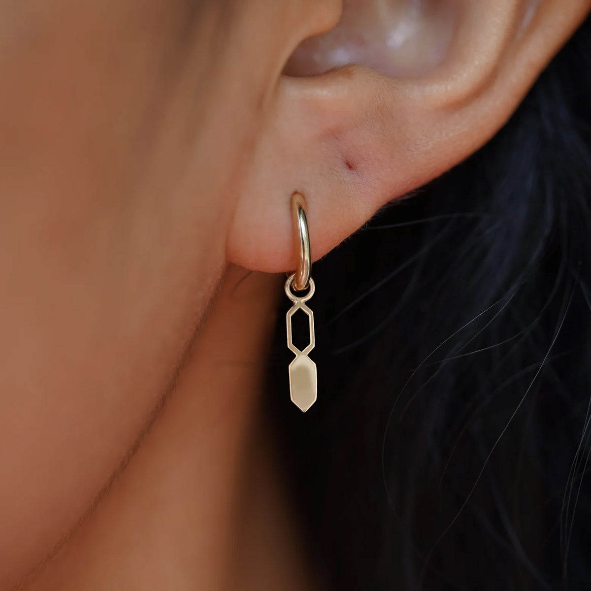 Close up view of a model's ear wearing a champagne gold Tanlah Charm on a Curvy Huggie Hoop