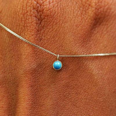 Close up view of a 14k champagne gold Turquoise Necklace draped across the back of a model's hand