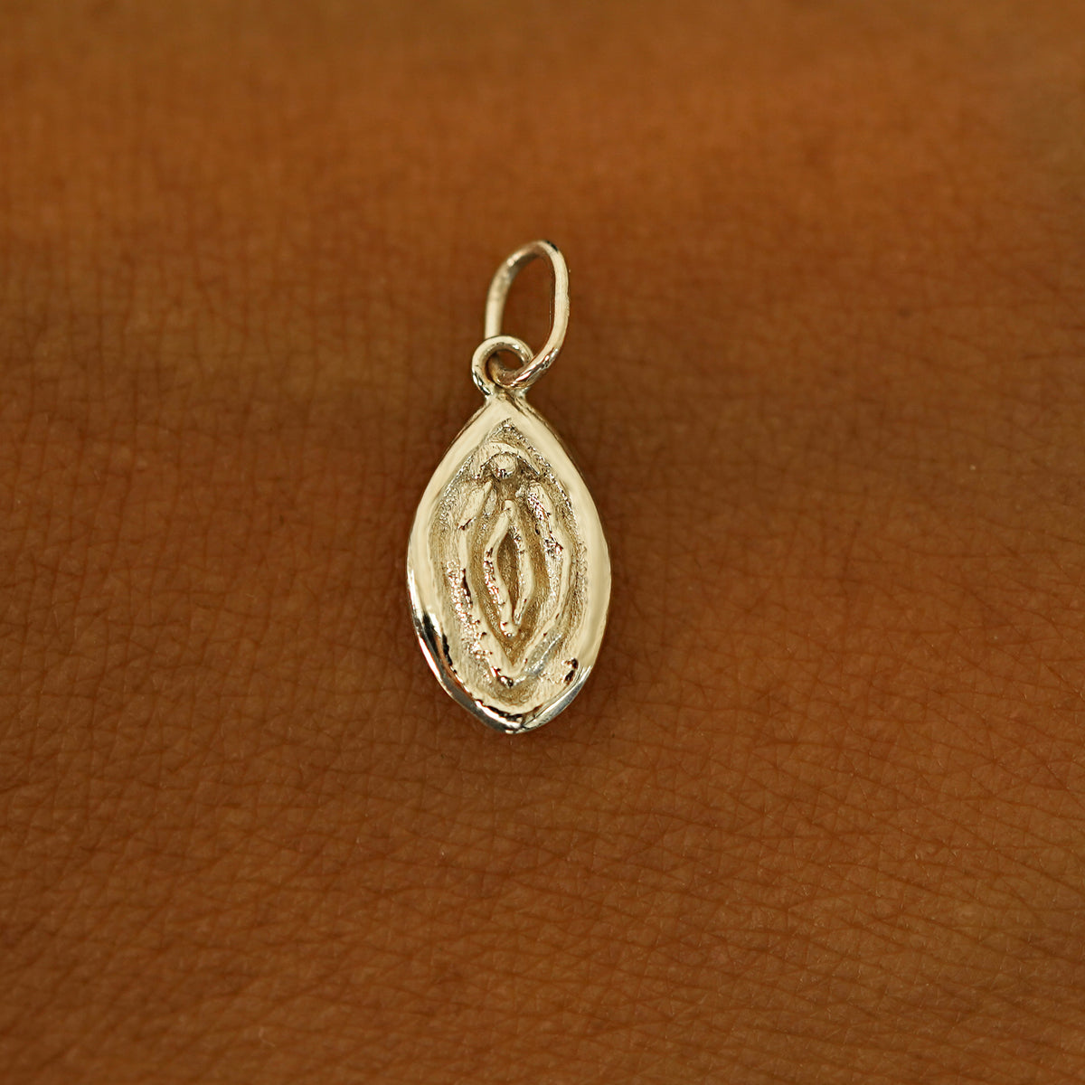 A solid 14k champagne gold Vulva Charm resting on the back of a model's hand