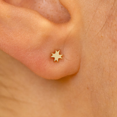 Close up view of a models ear wearing a 14k champagne gold 8 pointed star flatback piercing