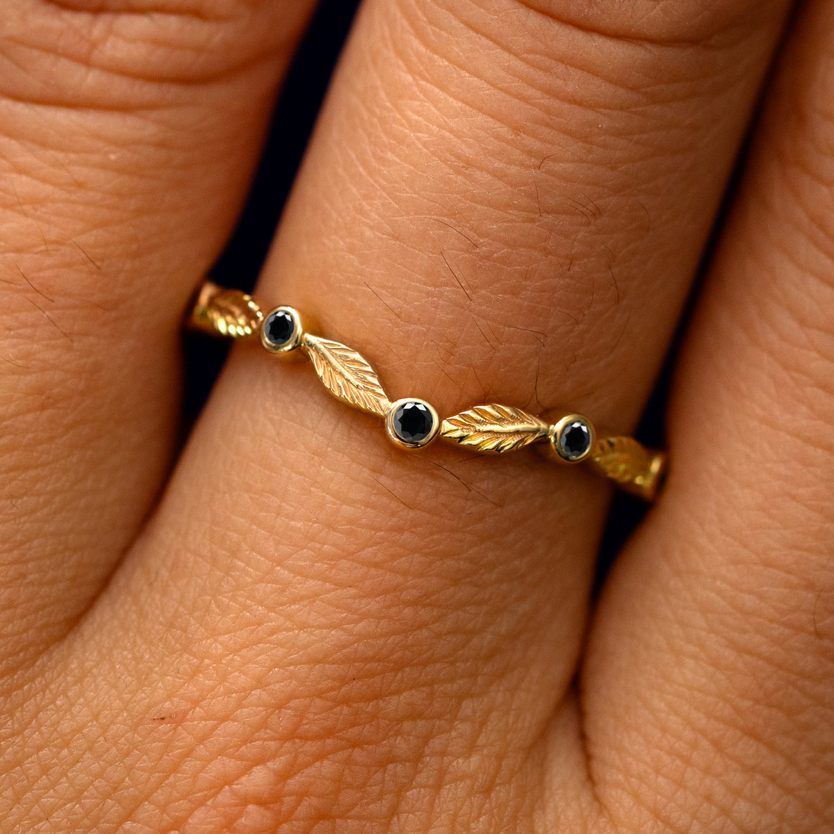 Close up view of a model's fingers wearing a 14k yellow gold Chevron Leaves and Black Diamonds Band