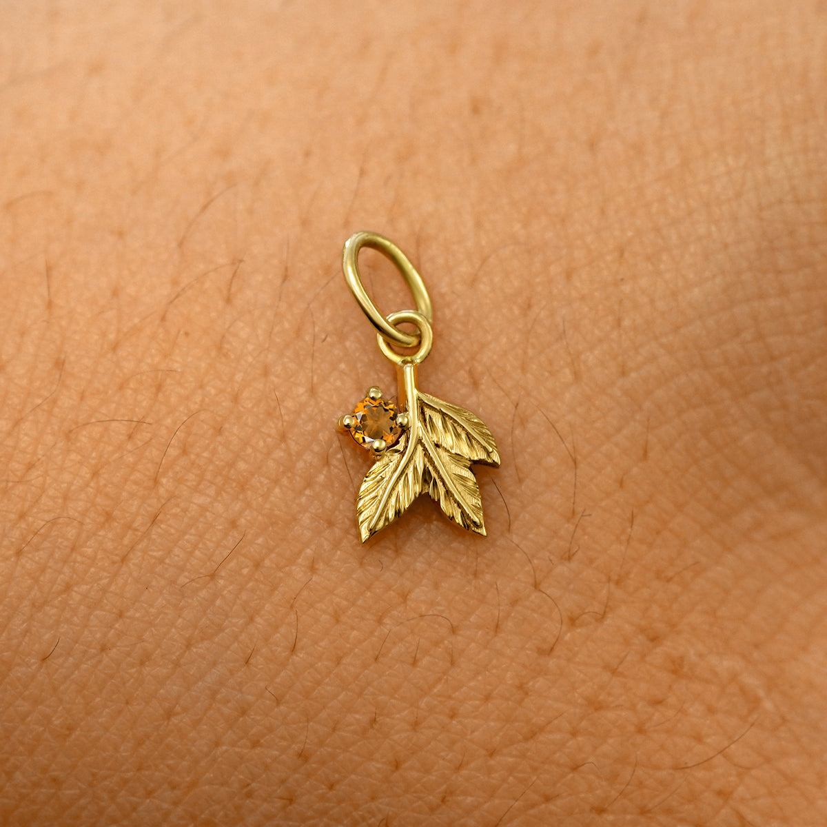 A solid 14k yellow gold citrine Gemstone 3 Leaves Charm resting on the back of a model's hand