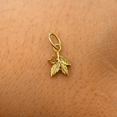 A solid 14k yellow gold citrine Gemstone 3 Leaves Charm resting on the back of a model's hand