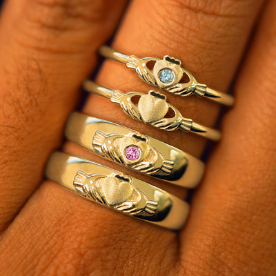 A finger wearing yellow gold Claddagh Ring, Gemstone Claddagh RIng, Claddagh Band and Gemstone Claddagh Band stacked 